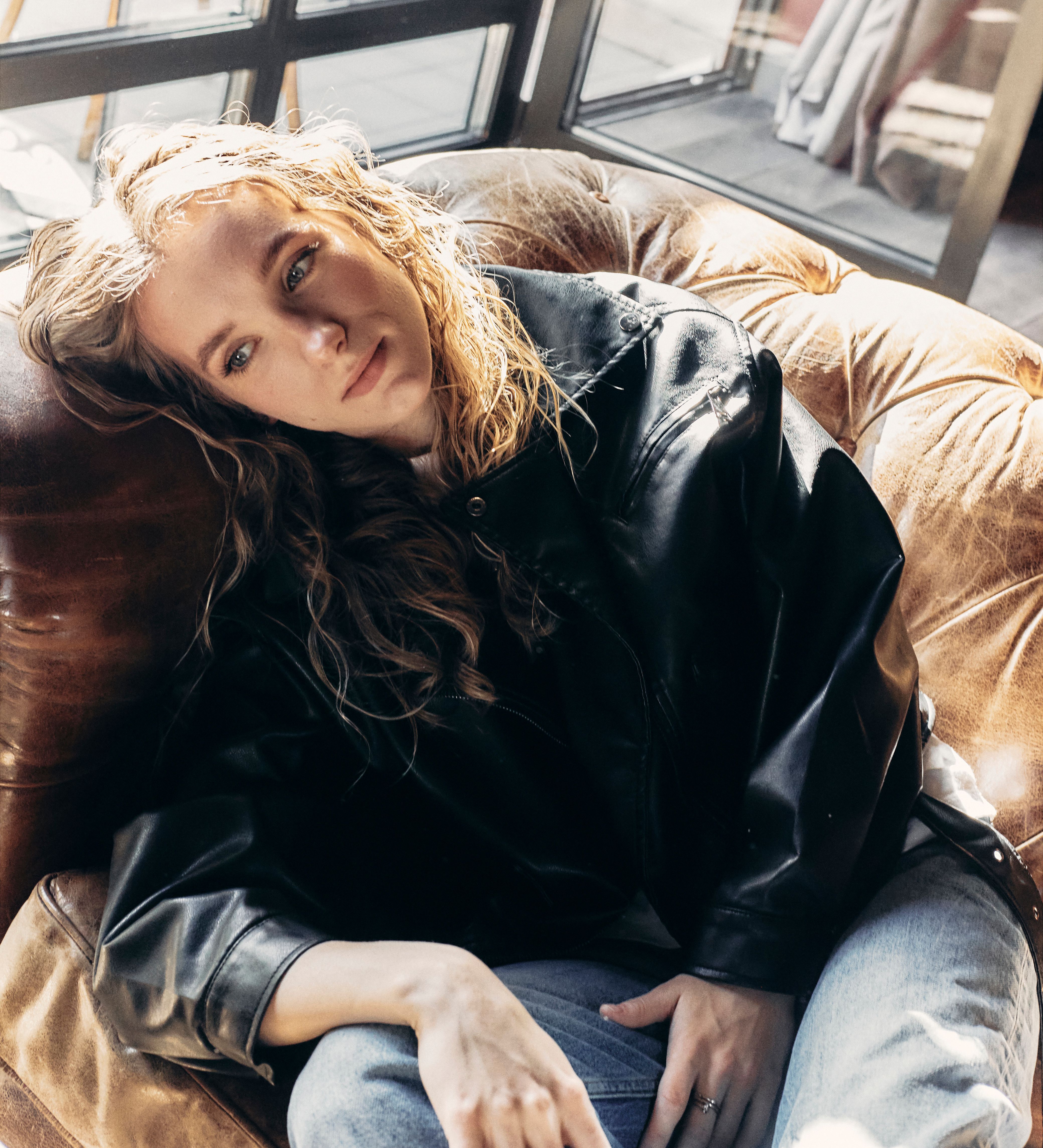 Young woman in a black leather jacket relaxing indoors on a sunny day.