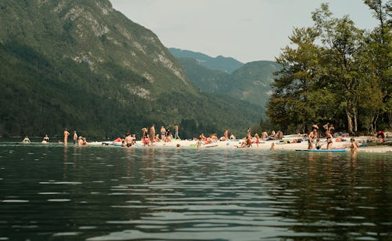 Crowded beach at Soča River with people enjoying summer activities surrounded by mountains.