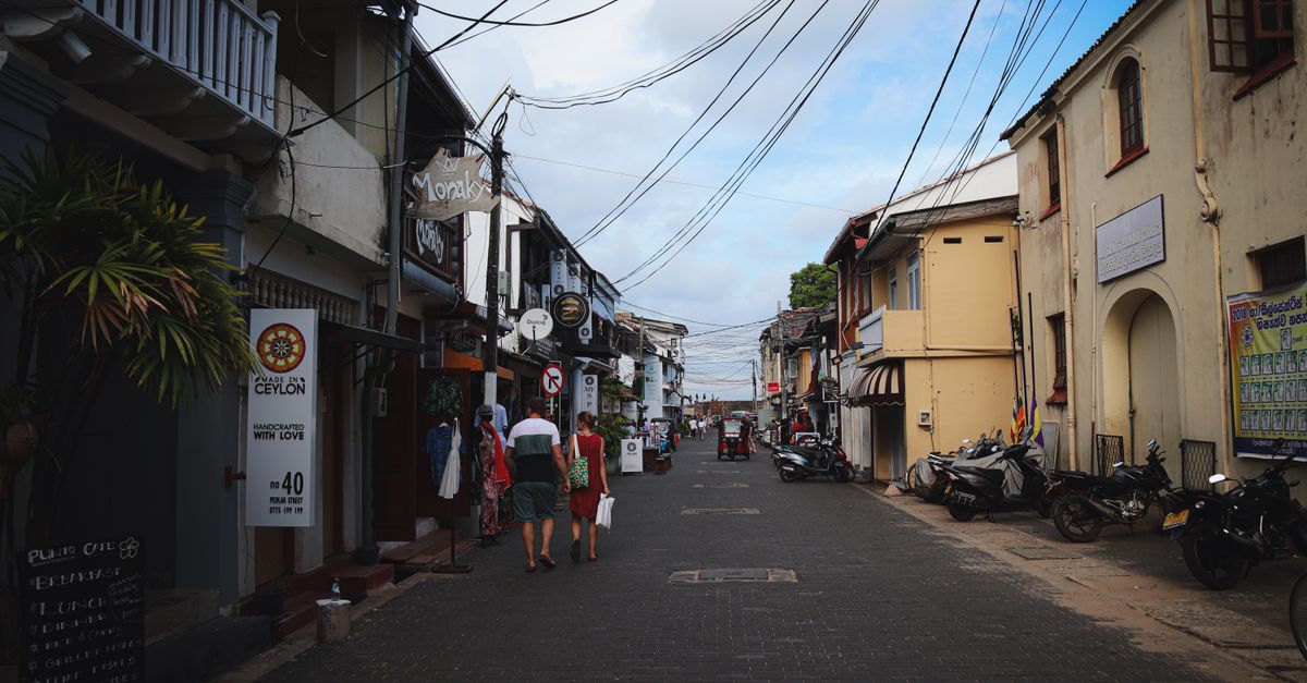 Historic street scene in Galle Fort, Sri Lanka with shops and pedestrians under a blue sky.