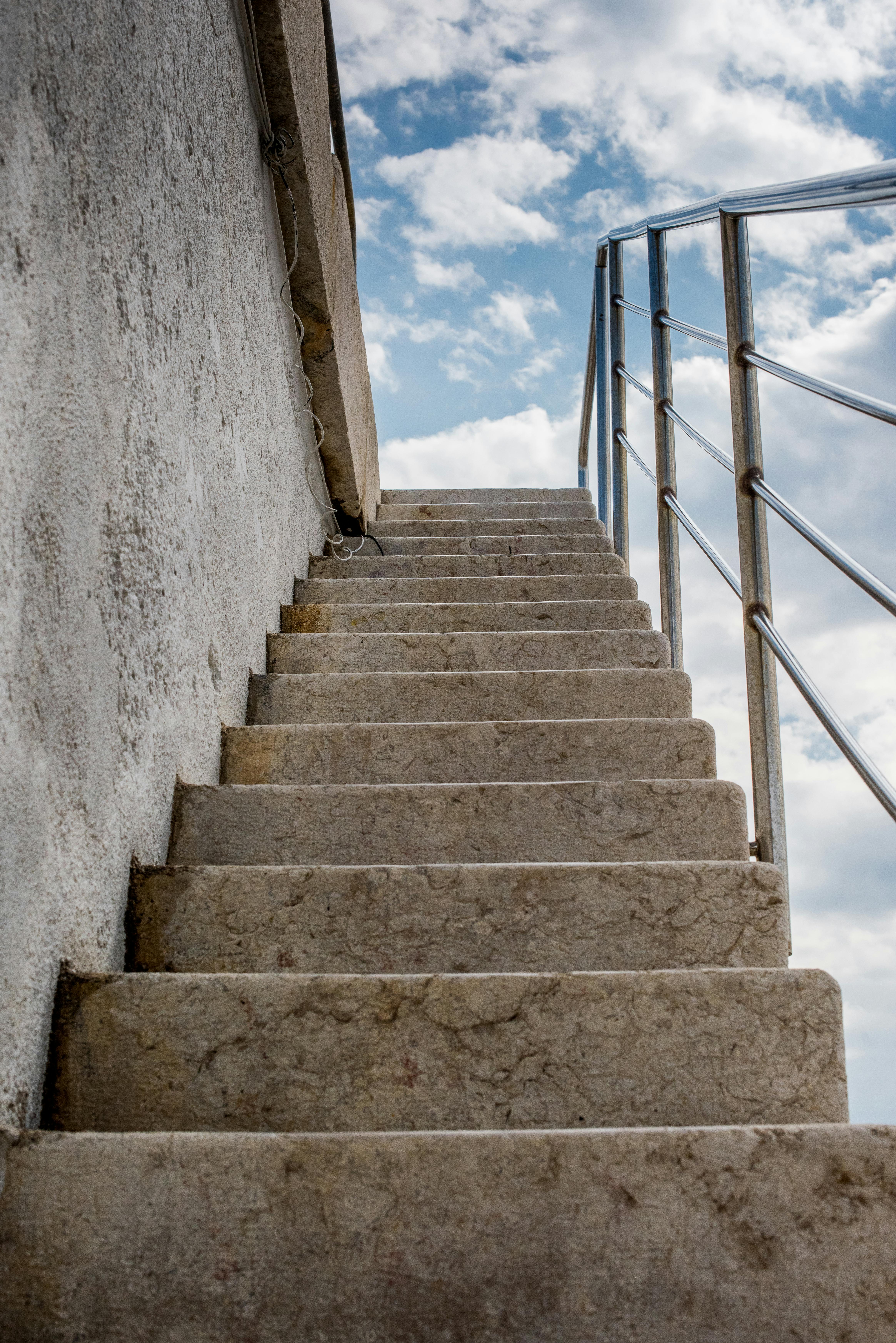 Stone staircase with railing leading upwards towards a cloudy blue sky.