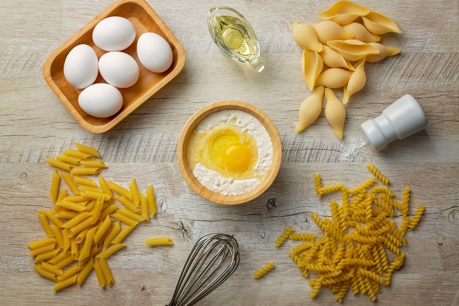 Photo by Marcelo Verfe on Pexels Flat lay of pasta ingredients including eggs, flour, and olive oil on a wooden surface. - Photo by Marcelo Verfe on Pexels