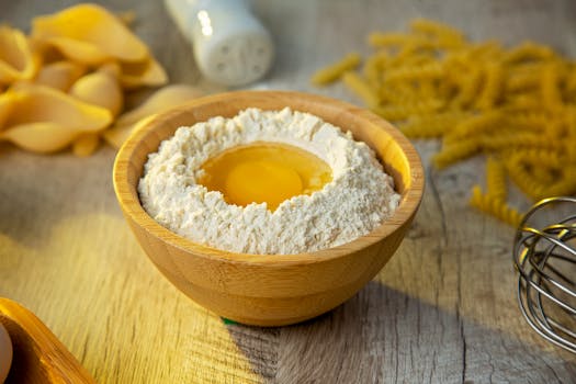 A wooden bowl with flour and egg yolk staged for making homemade pasta.
