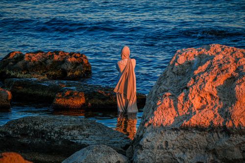Free A woman in traditional clothing stands alone at the rocky shore of the Caspian Sea in Aktau, Kazakhstan. Stock Photo