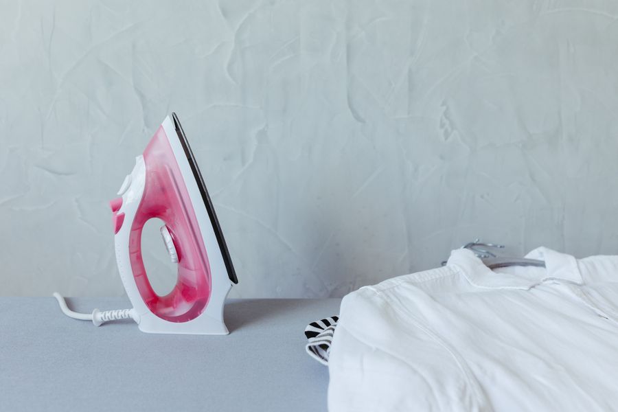 A vibrant pink iron next to a neatly folded white shirt on an ironing board against a textured wall.