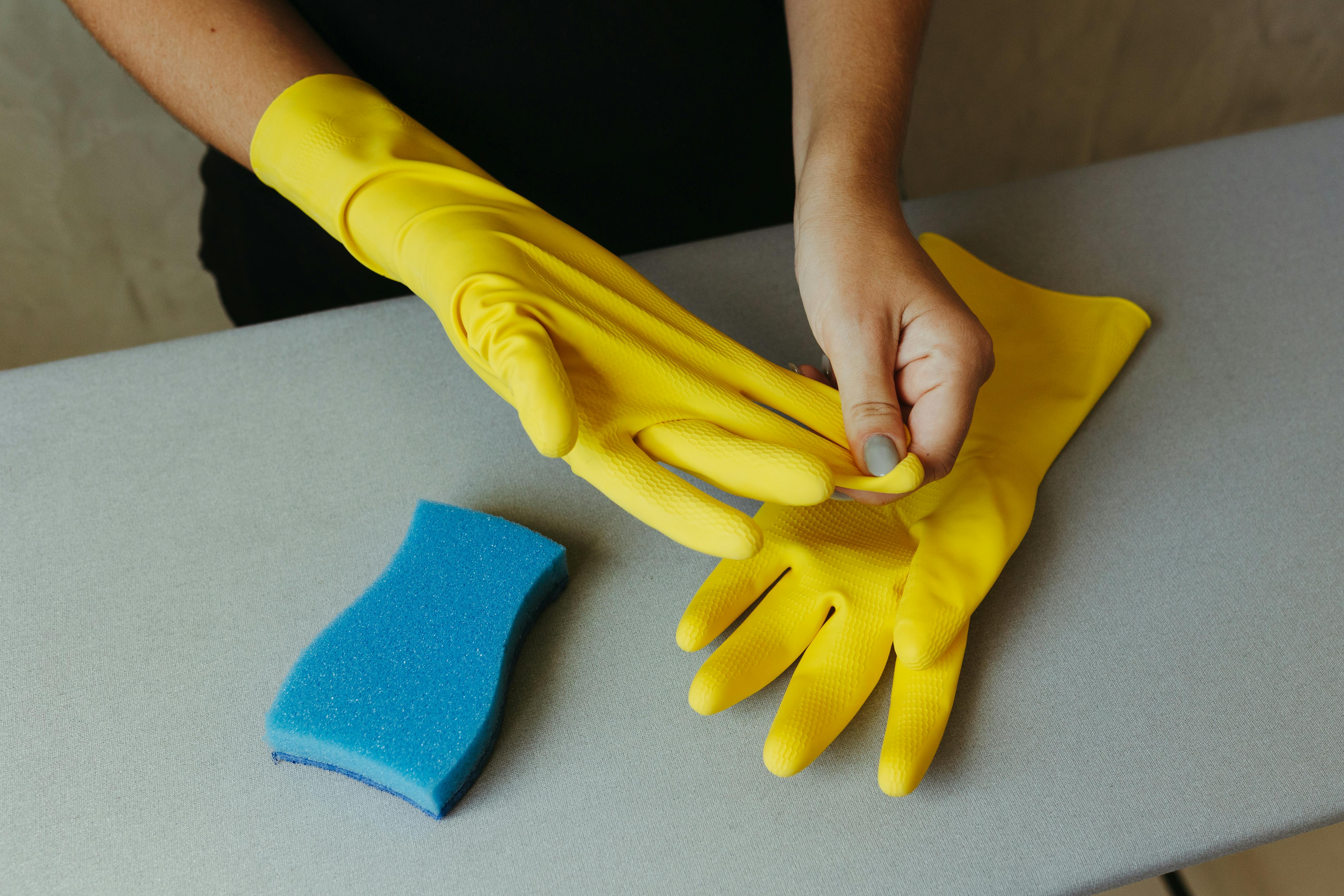 Free Individual putting on yellow rubber gloves with a blue sponge nearby. Stock Photo