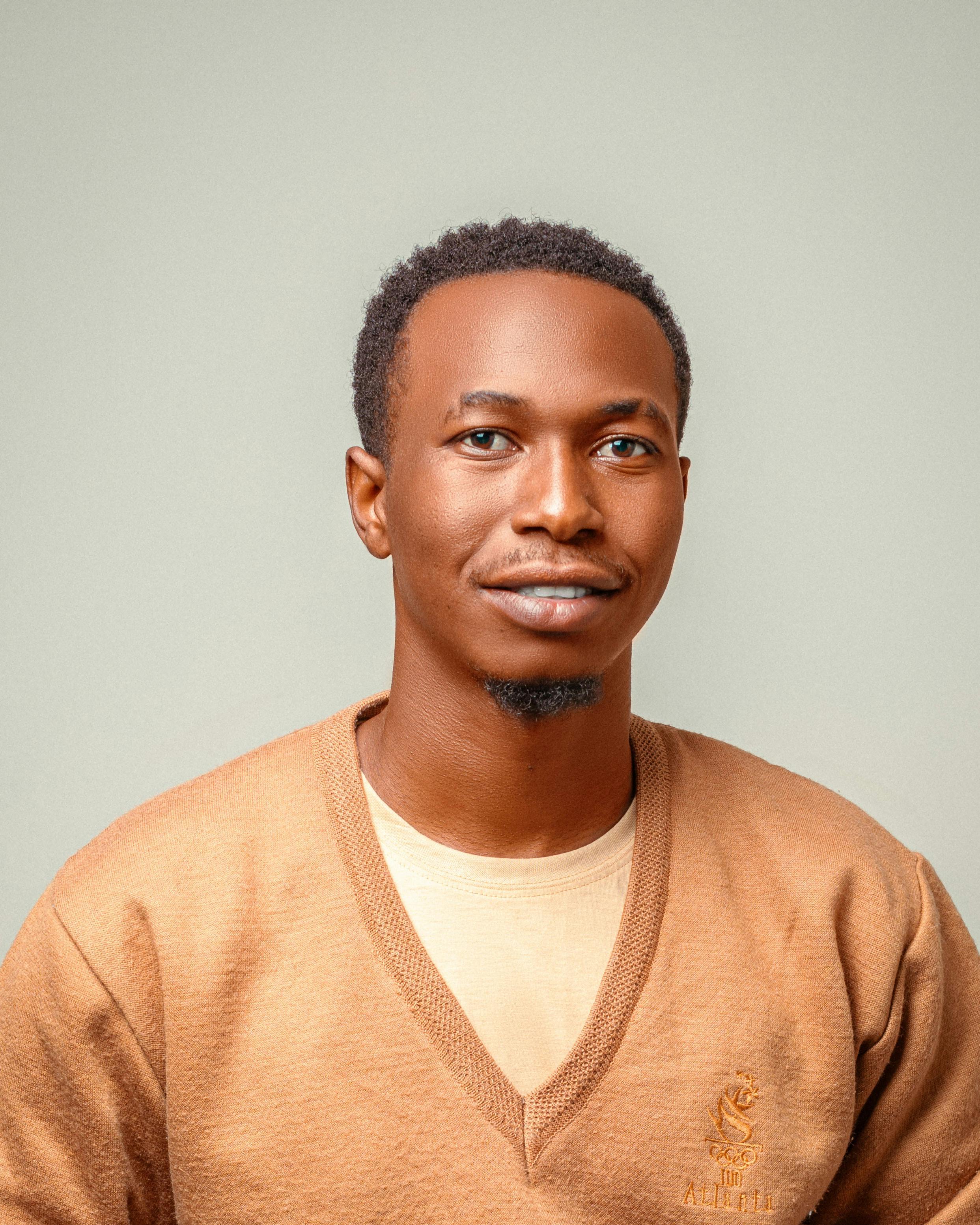 A friendly portrait of a man with a warm expression wearing a brown sweater, against a soft background.
