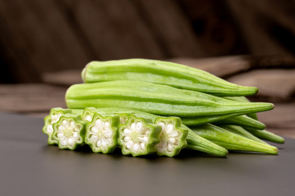 Fresh okra pods arranged on a dark surface, showing ridged texture`