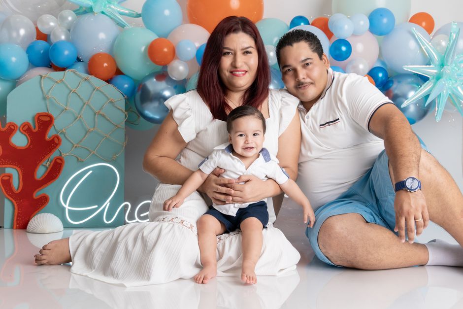 A joyful family portrait celebrating a child's first birthday with colorful balloons.