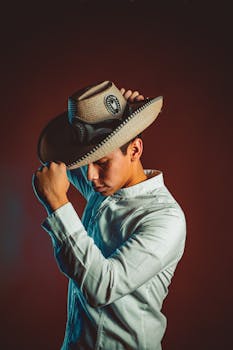 A man in traditional Mexican attire with a cowboy hat poses against a dark background.