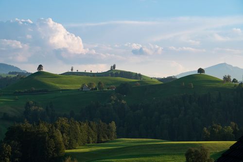 Free Beautiful rolling green hills under a cloudy blue sky capturing serene natural scenery. Stock Photo