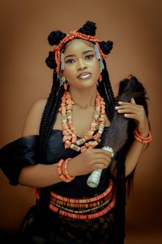 Portrait of a Nigerian woman in vibrant traditional attire holding a ceremonial piece.