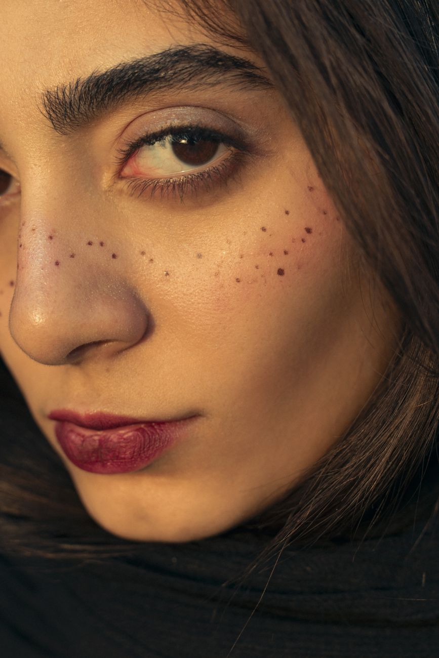 Artistic closeup of a woman highlighting freckles with dramatic makeup and red lipstick.
