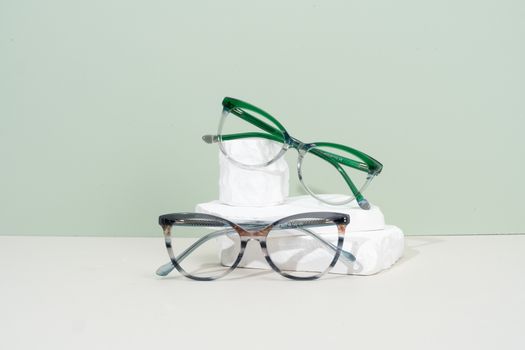 Minimalist eyeglasses display with green and transparent frames on a pastel background.