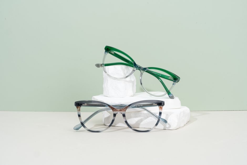 Minimalist eyeglasses display with green and transparent frames on a pastel background.