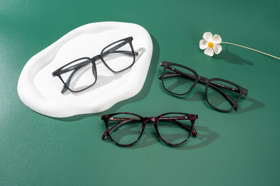 Modern eyeglasses arranged on a green surface with delicate floral decor.