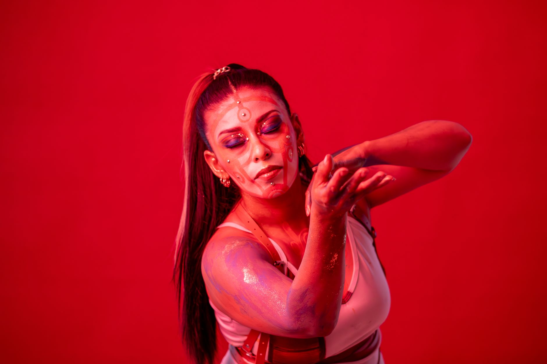 Woman with artistic face paint poses gracefully against a vivid red background.