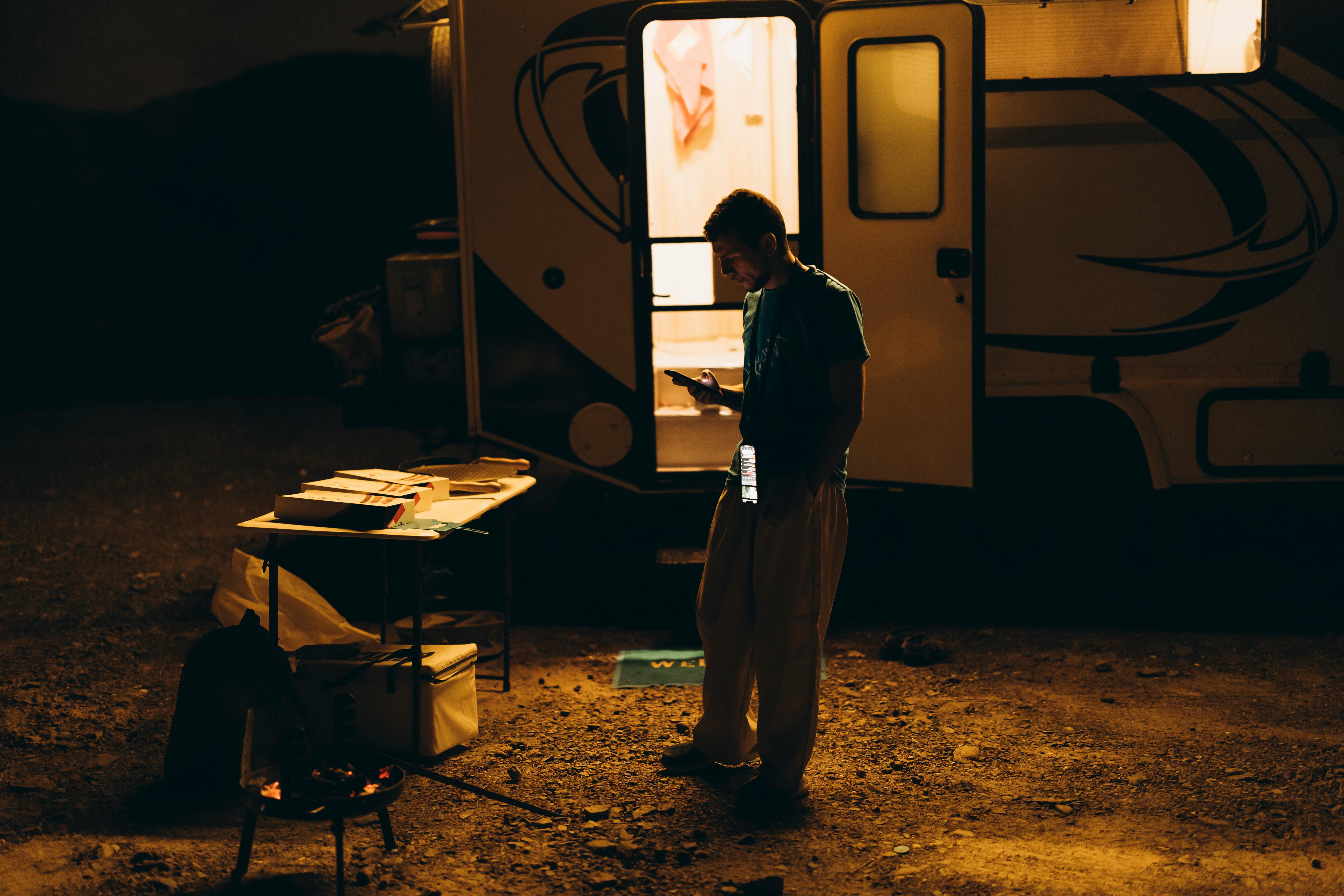 Free A moody nighttime scene of a camper using a phone outside a trailer in Showkah, UAE. Stock Photo