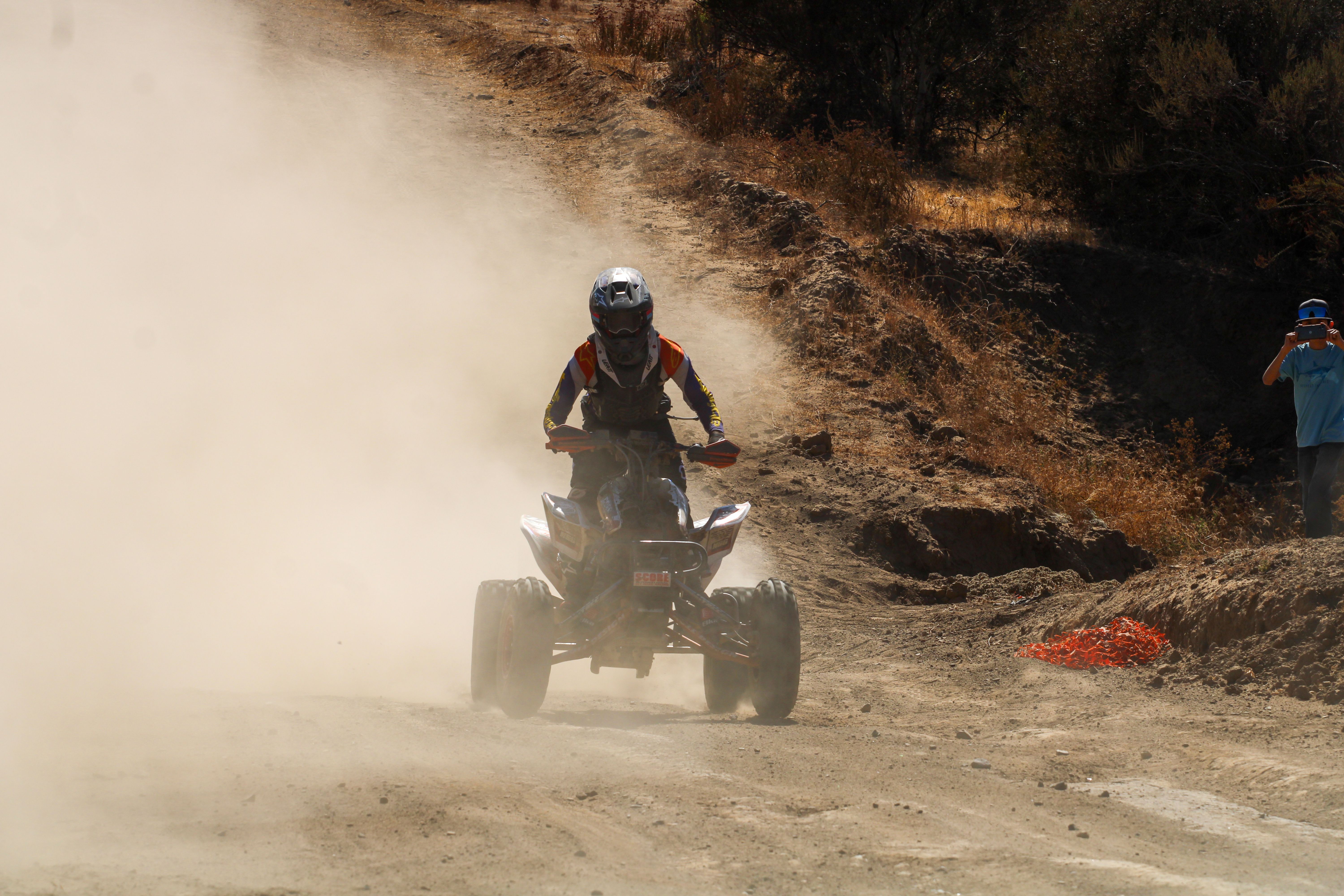 Rider on quad bike kicking up dust on rugged outdoor trail, perfect for adventure sports