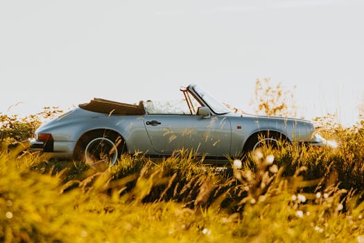 Vintage convertible car parked in a sunlit meadow, capturing a nostalgic summer feel.