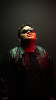 Portrait of a man in a leather jacket, wearing sunglasses, captured with moody and dramatic lighting in a studio.