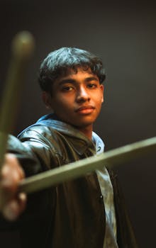 Cinematic portrait of a young drummer holding drumsticks in warm lighting.