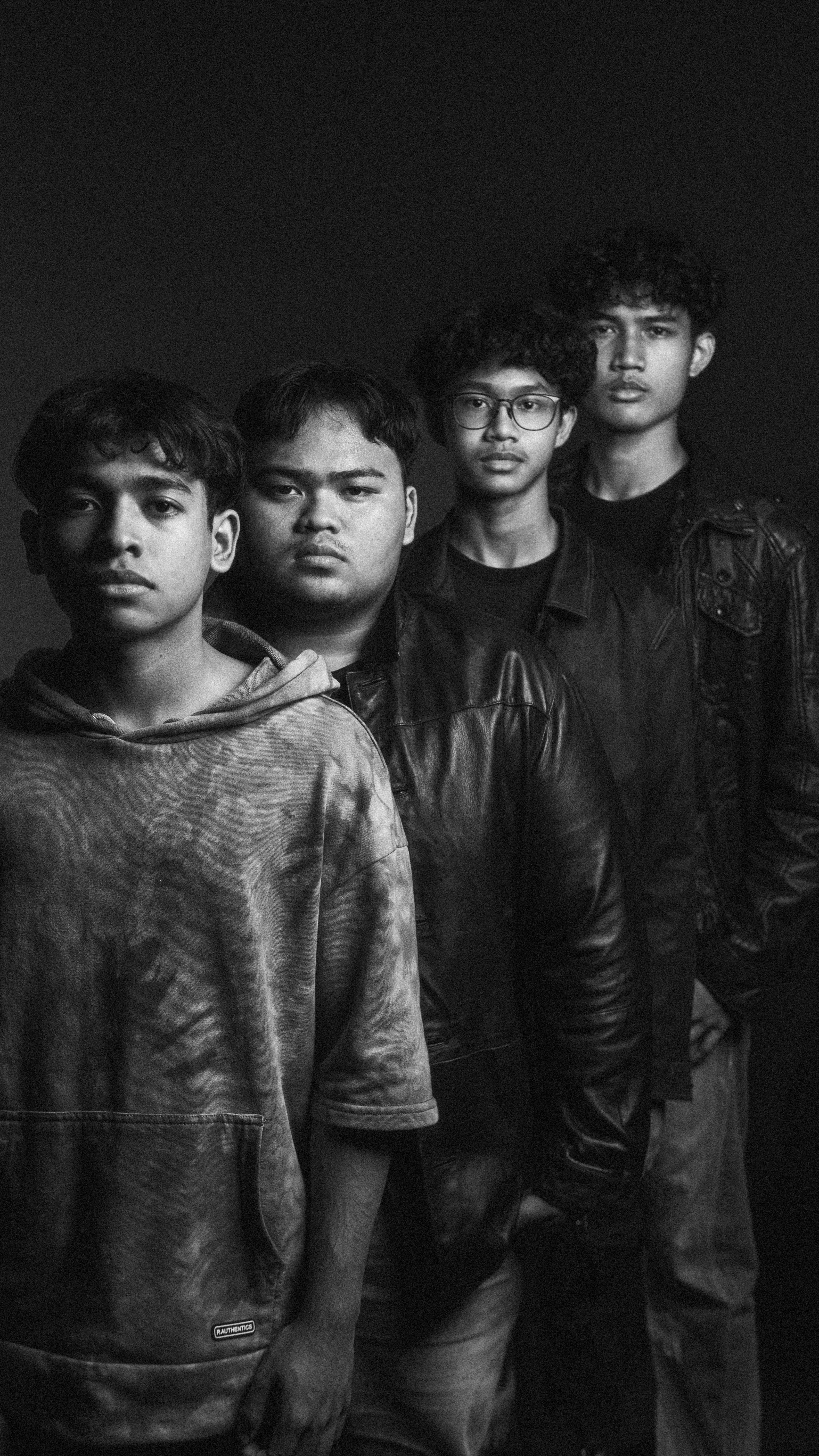 Moody black and white portrait of four teen band members in a studio setup.