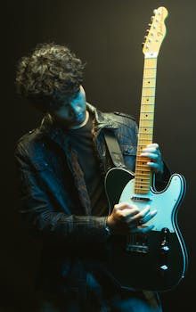 Portrait of a young musician holding an electric guitar in moody studio lighting.