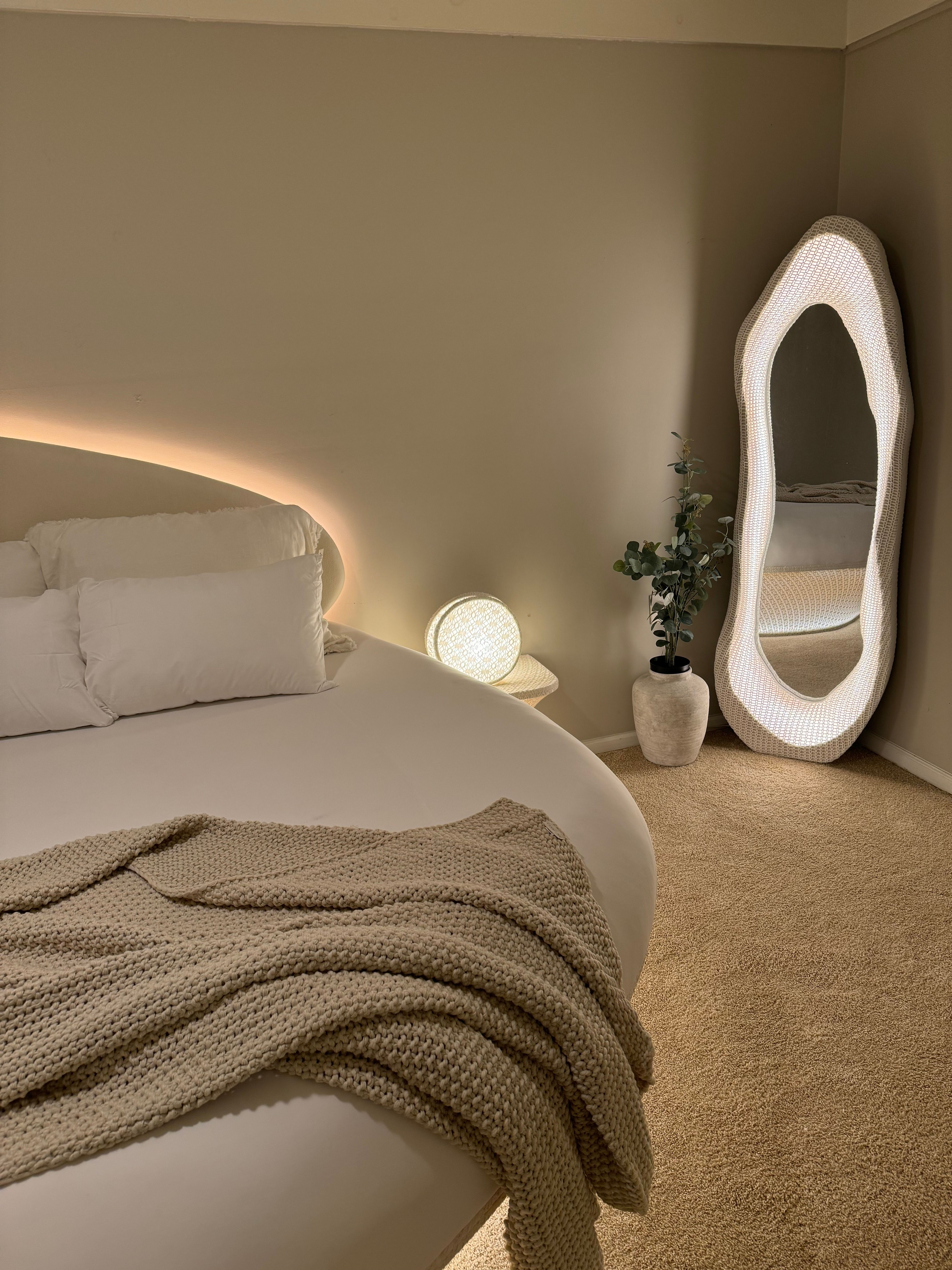 Quarto em tons neutros com iluminação indireta e espelho de corpo inteiro