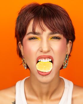 Playful portrait of woman biting a lemon with bold orange backdrop.