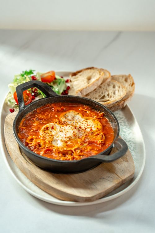 Free Savory shakshuka served in a skillet with fresh salad and bread, perfect for breakfast. Stock Photo