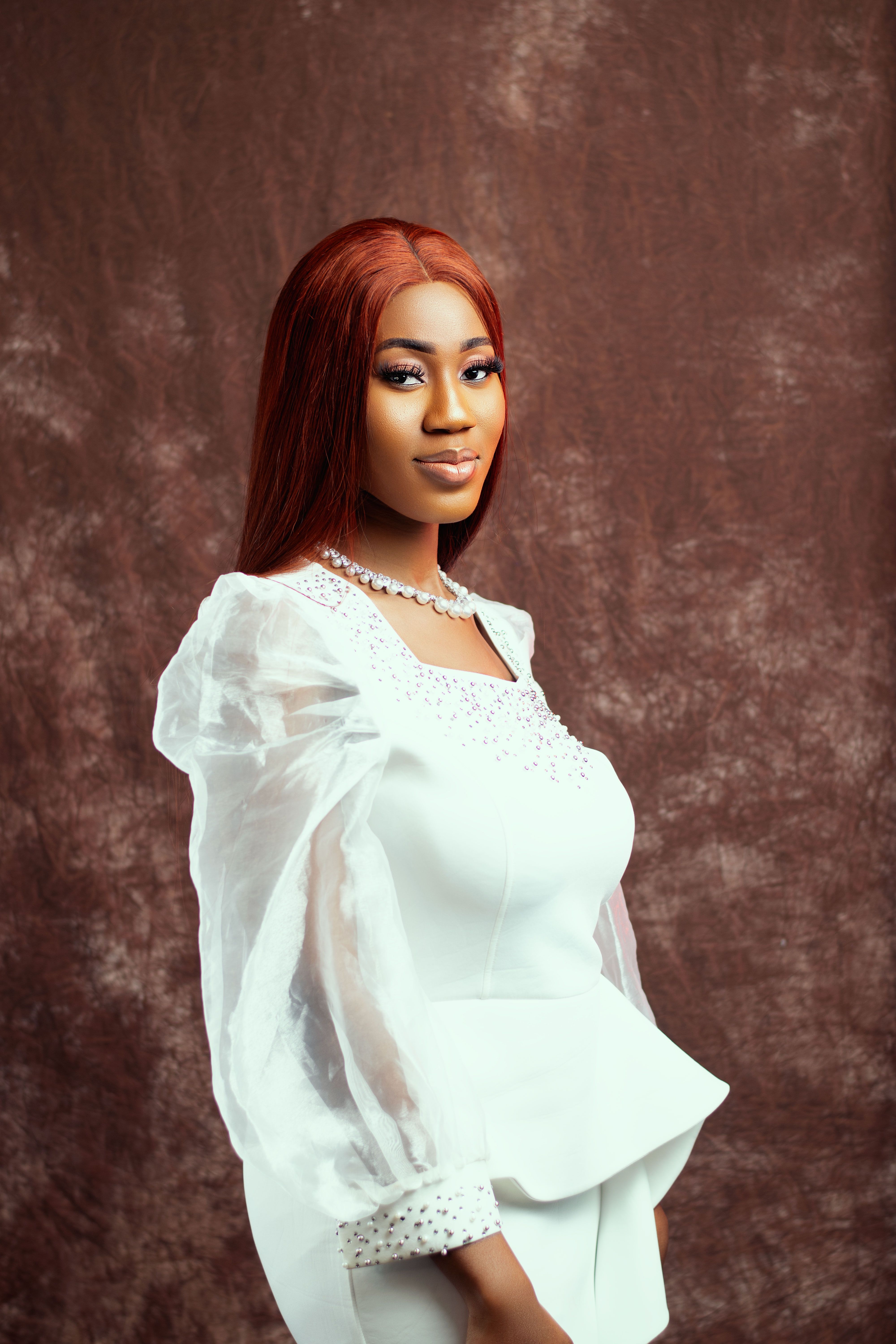 Beautiful young woman in a white bridal dress with orange hair posing in a studio setting.