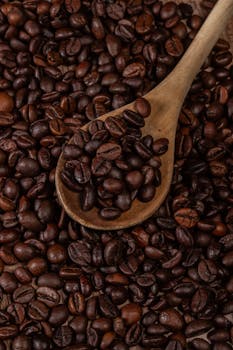 Close-up of roasted coffee beans with a wooden spoon, perfect for coffee-themed content.