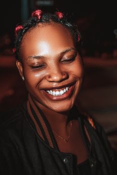 A joyful woman with braided hair, smiling brightly under night lights.