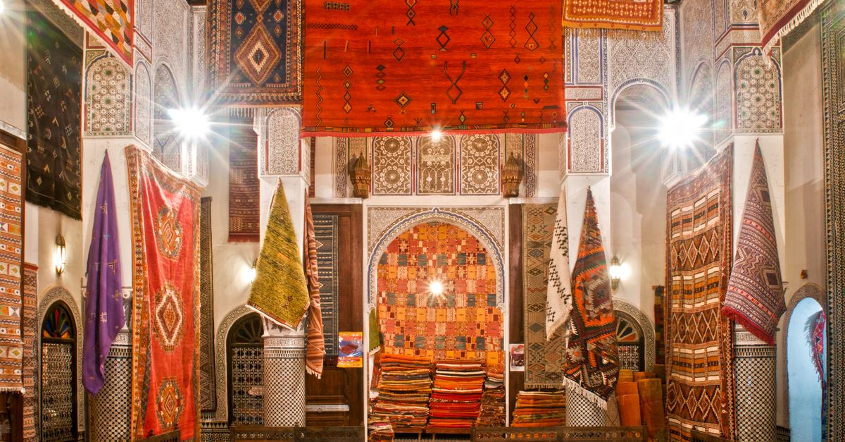 Colorful display of Moroccan rugs in a traditional market in Fès, showcasing intricate patterns and warm tones.
