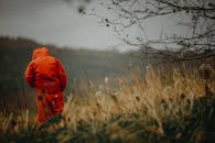 身穿橙色夹克的人独自站在田野里，从后面被抓获