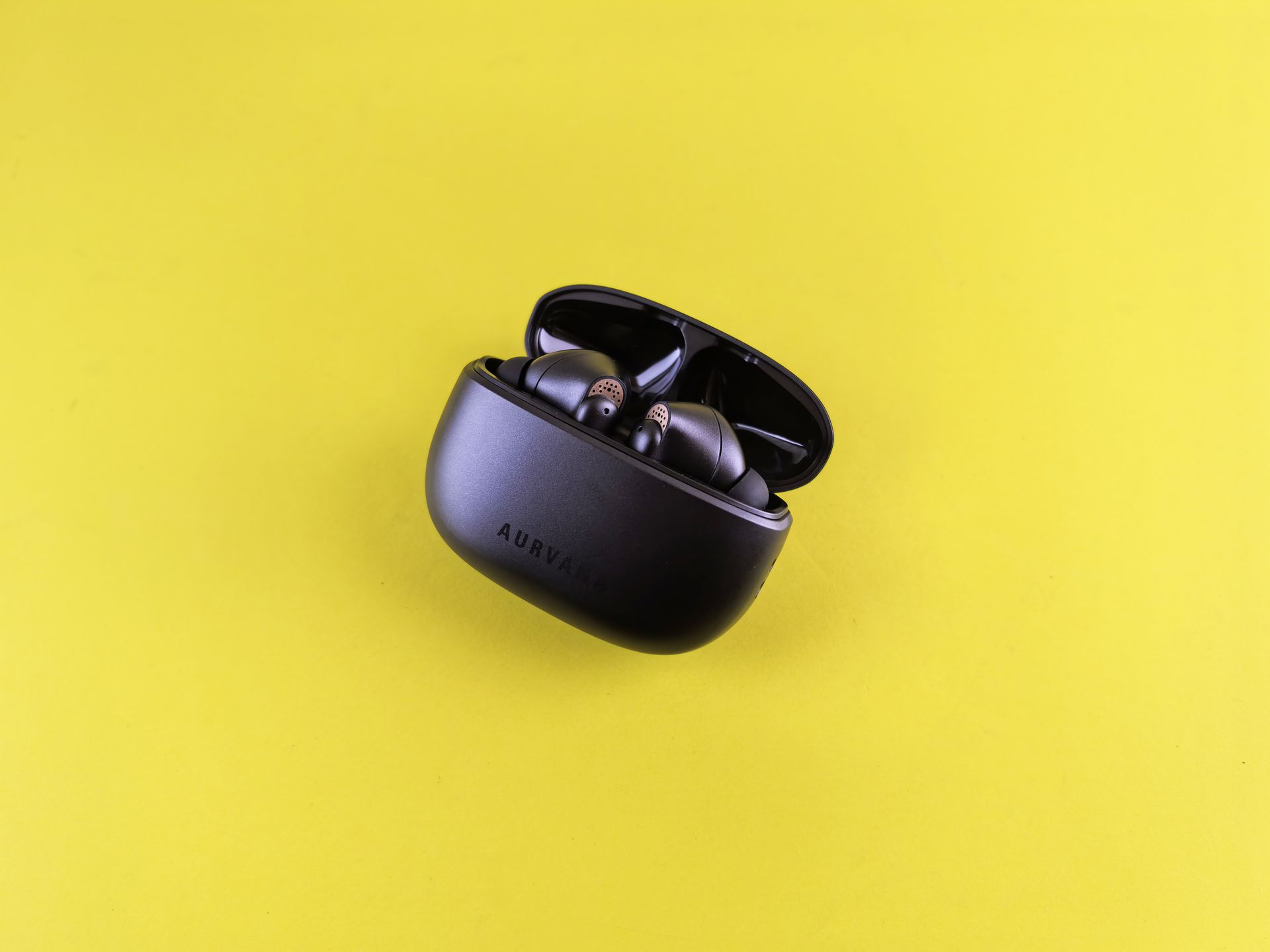 Close-up of modern black wireless earbuds in charging case on a vibrant yellow background.