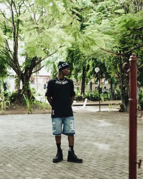 Casual young man standing outdoors among lush green trees.