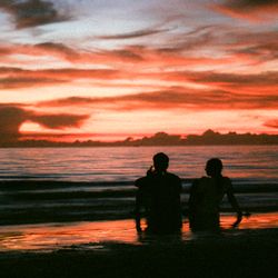 Two people silhouetted against a sunset on the shore — photo by travelers_tw on Pexels