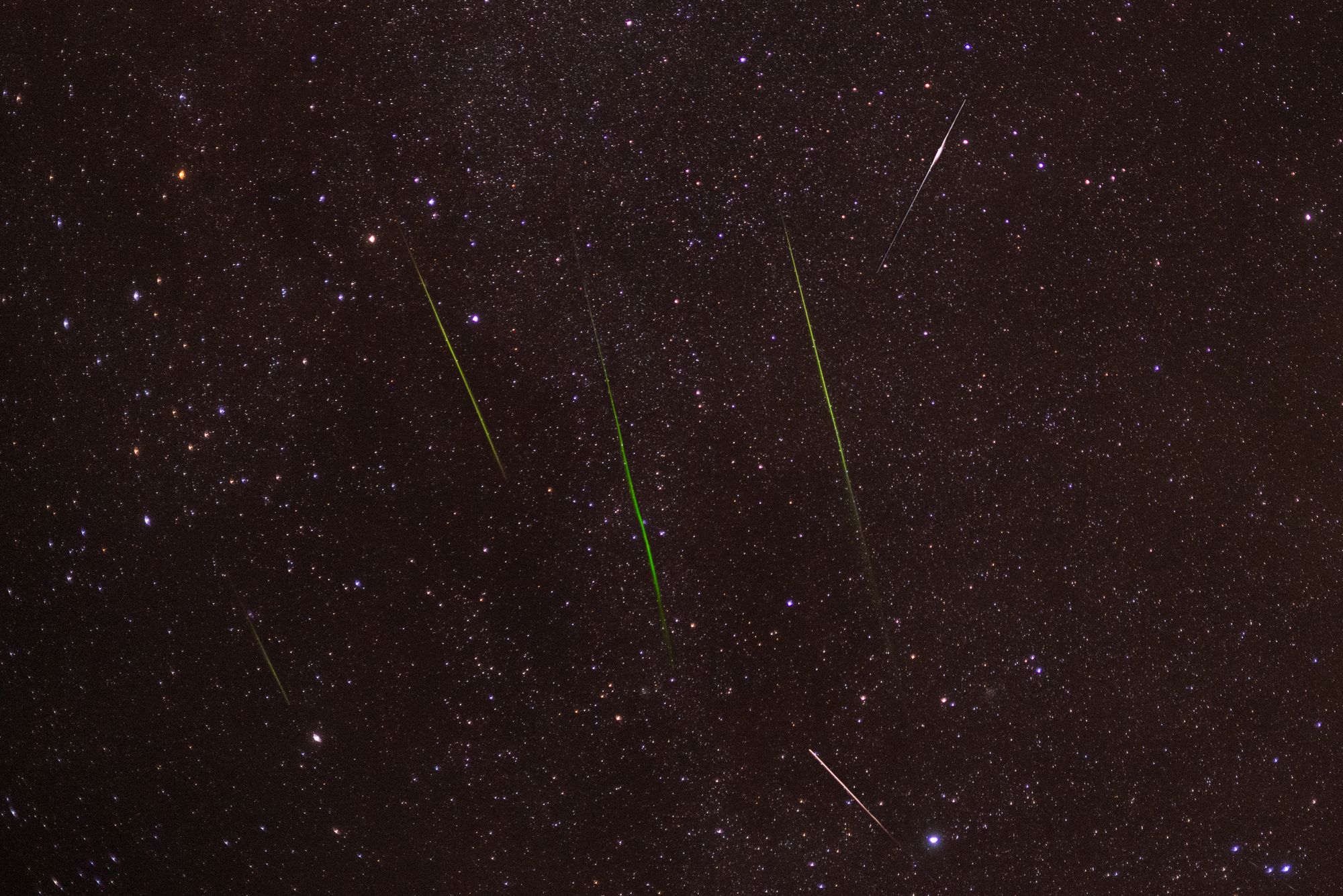 Bright meteors streak across a starry night sky during a captivating shower.