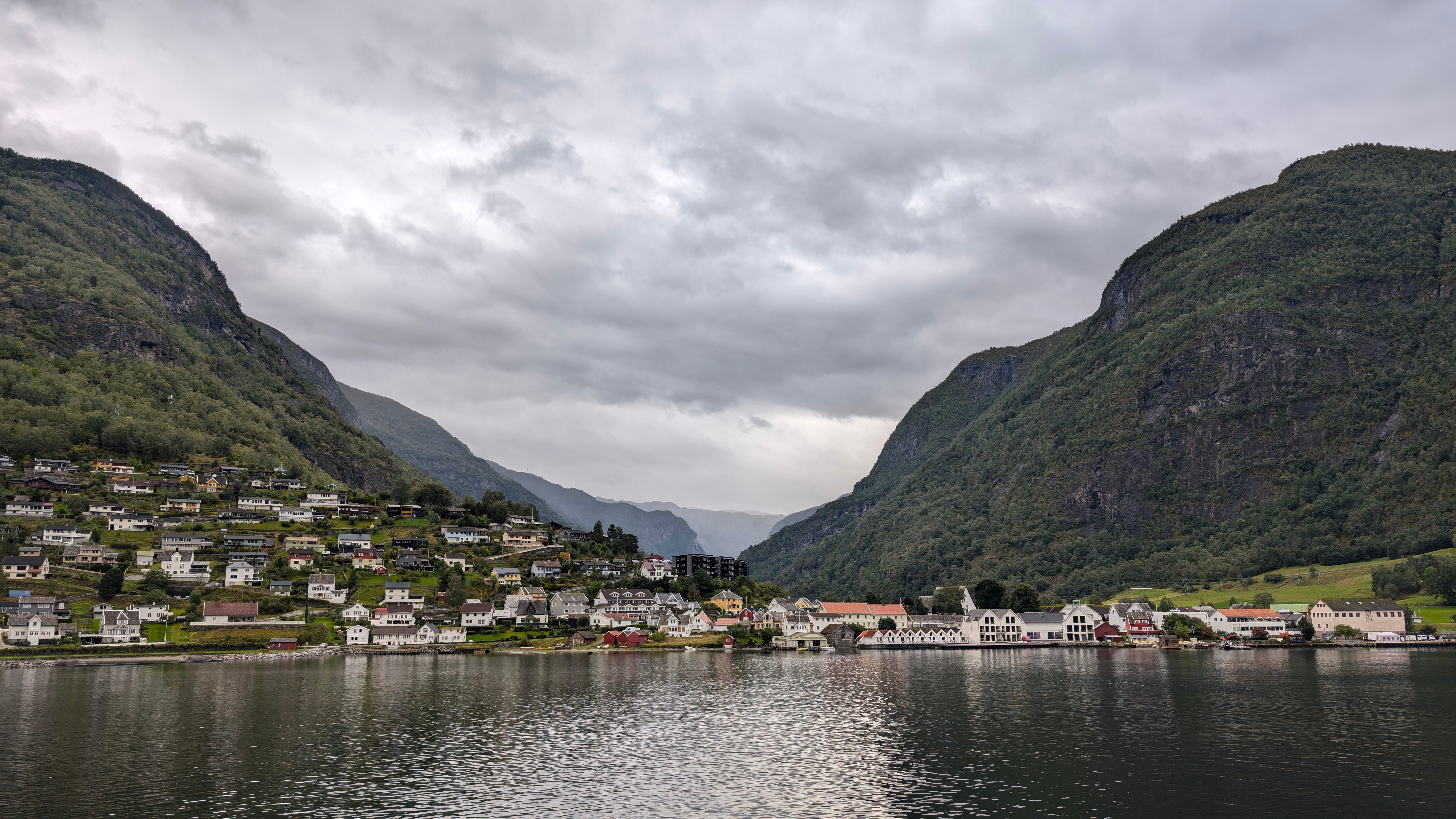 Picturesque view of Bergen, Norway with houses, fjord, and mountains under cloudy skies.