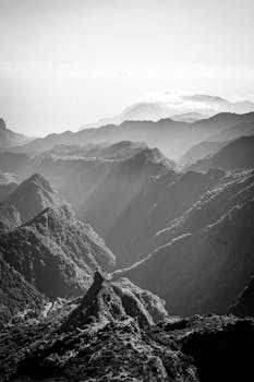 A breathtaking black and white landscape of mountain ranges with mist and dramatic lighting.