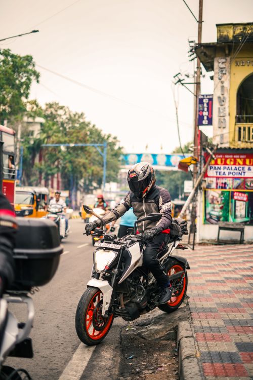 Free A motorcyclist waits at the curb on a busy urban street, surrounded by traffic. Stock Photo
