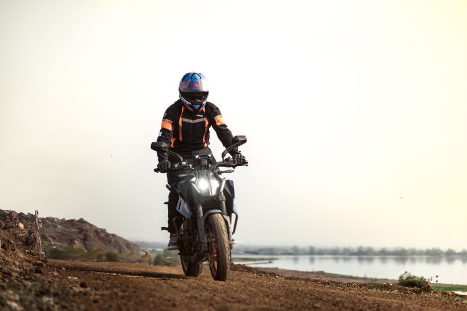 A motorcyclist riding off-road on a KTM near a scenic lake with a helmet and protective gear.