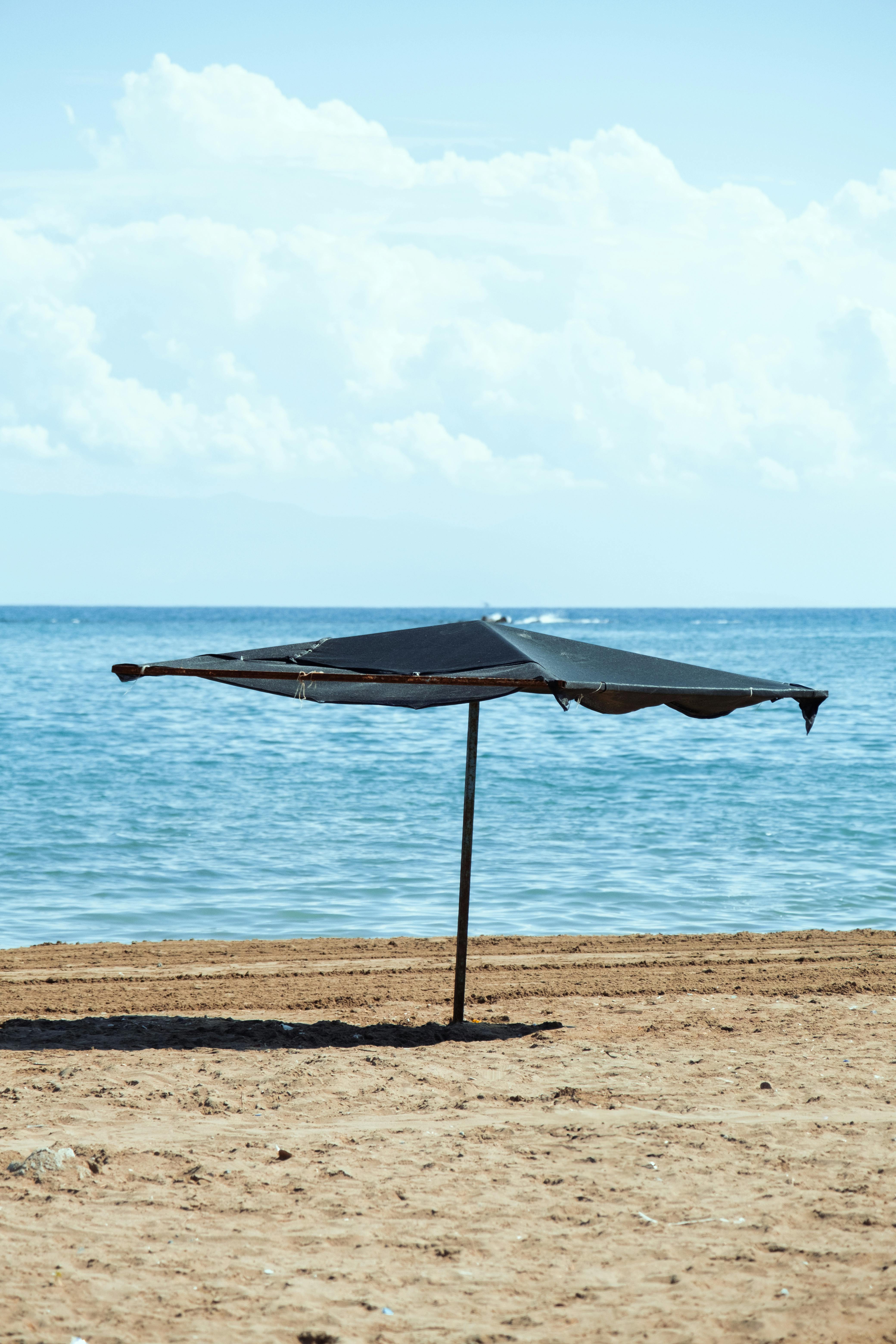 A lone beach umbrella on a sandy shore with a calm sea and clear sky background.