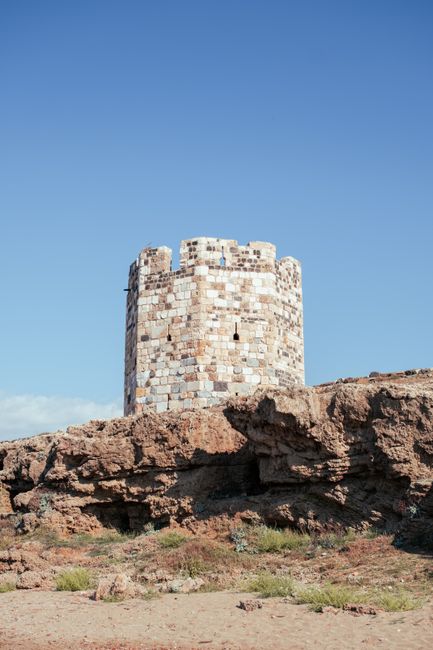 Majestic ancient stone tower atop a rugged, rocky cliff under a clear blue sky.
