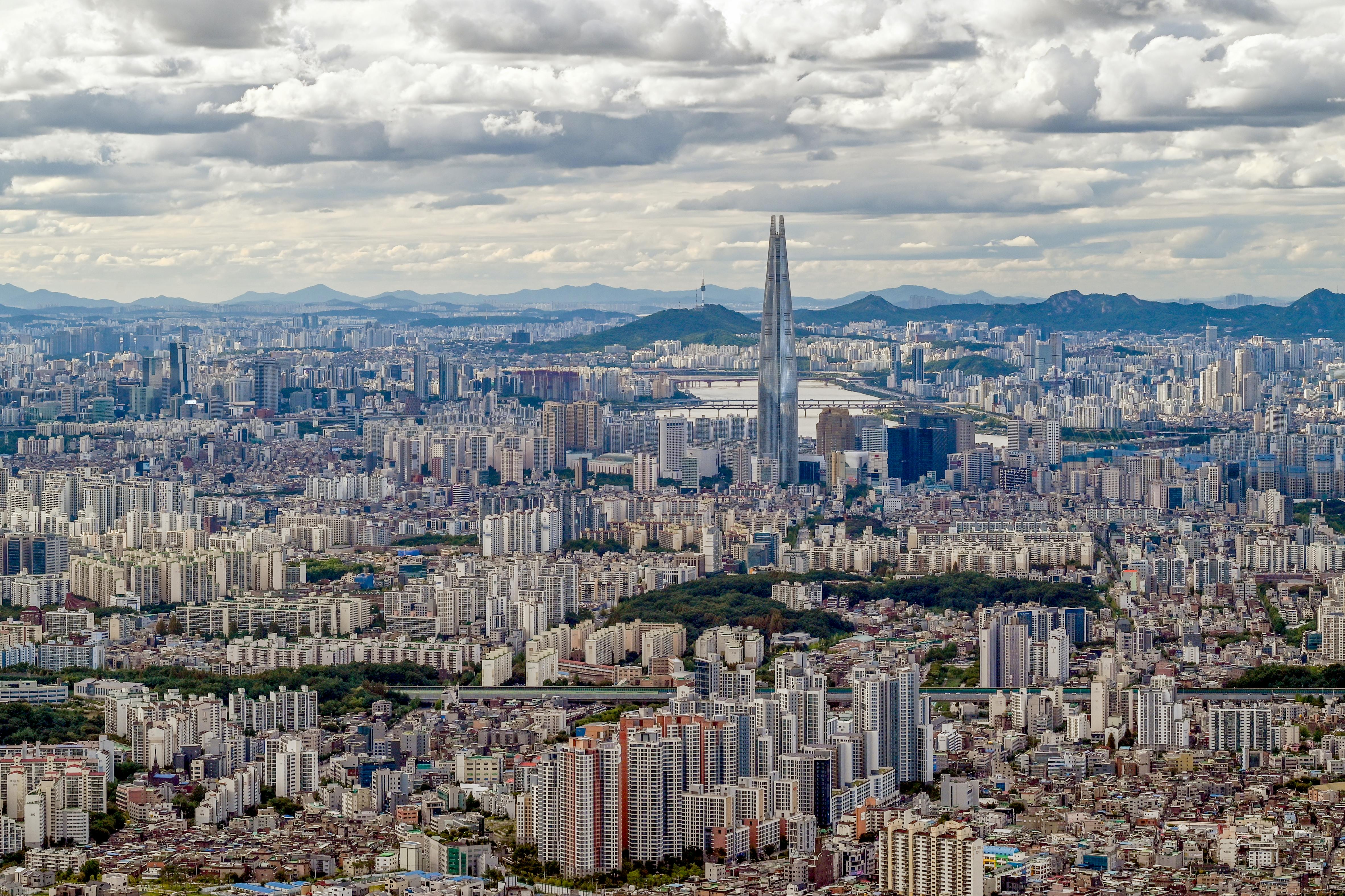 Panoramic aerial image of Seoul featuring the iconic Lotte World Tower under cloudy skies.