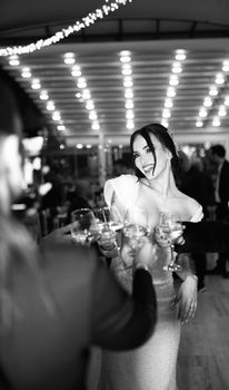 Joyous bride toasting at an indoor wedding reception in black and white.