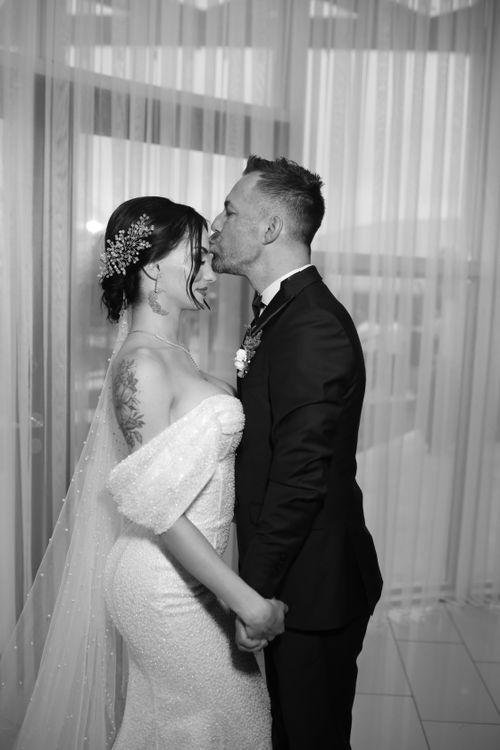 Free Romantic black and white photo of a wedding couple sharing a tender kiss indoors. Stock Photo
