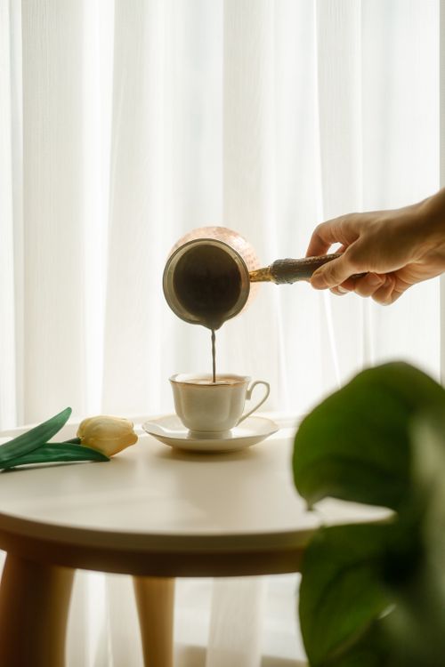Free Serene morning scene with coffee being poured into a cup near a tulip on a table. Stock Photo