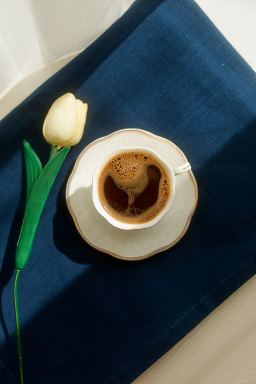 Free A delicate coffee cup with a tulip on a blue cloth, captured in bright daylight. Stock Photo